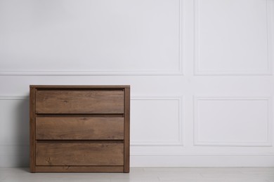 Photo of Wooden chest of drawers near white wall indoors, space for text