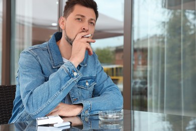 Handsome man smoking cigarette at table in outdoor cafe