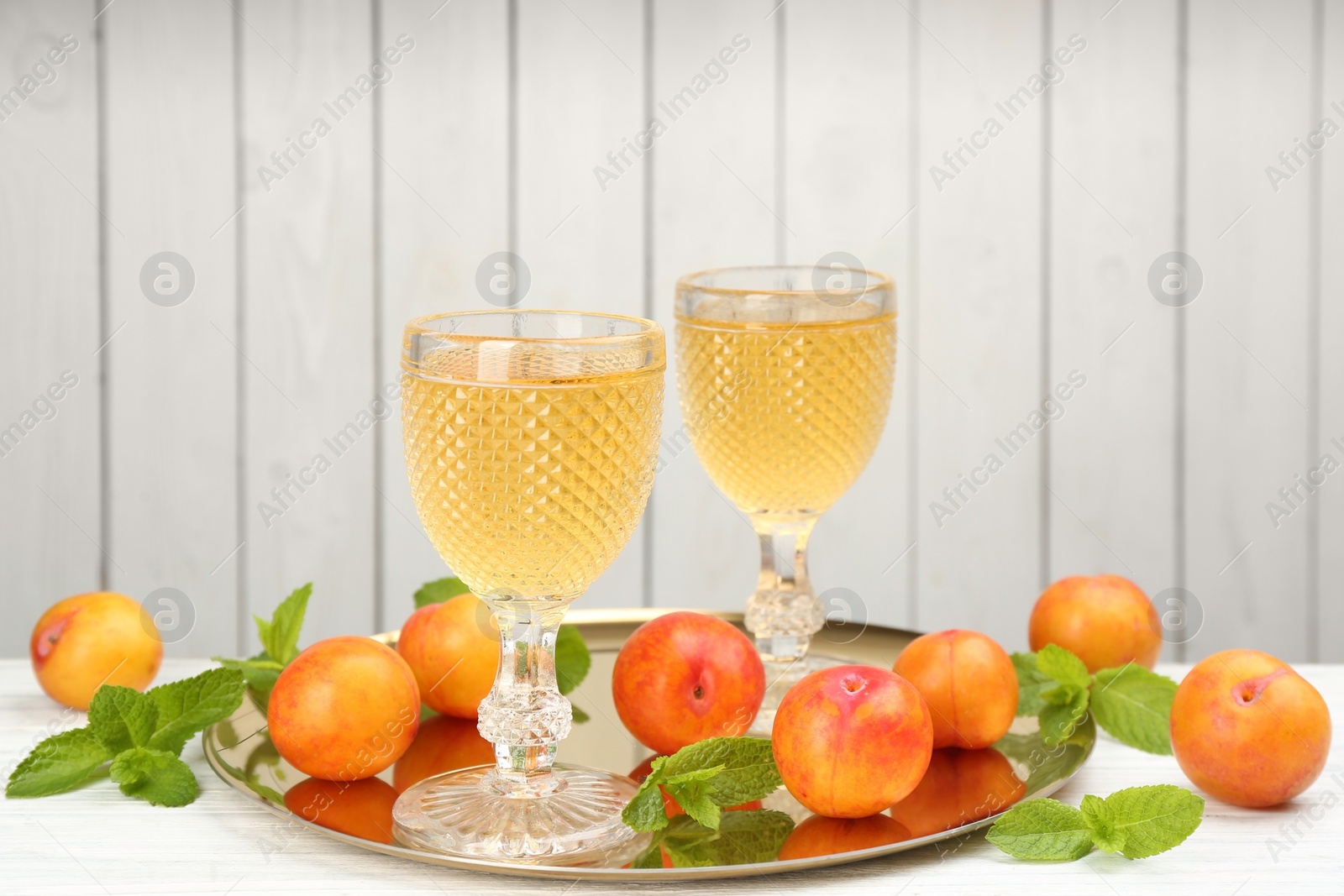 Photo of Delicious plum liquor, ripe fruits and mint on table against white background. Homemade strong alcoholic beverage