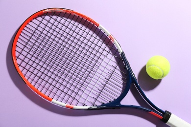 Photo of Tennis racket and ball on violet background, flat lay. Sports equipment