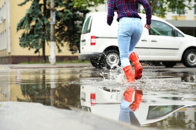 Woman with rubber boots running in puddle, closeup. Rainy weather