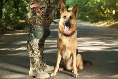 Photo of Man in military uniform with German shepherd dog outdoors, closeup view