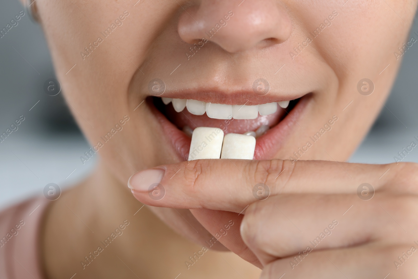 Photo of Woman putting chewing gums into mouth on blurred background, closeup