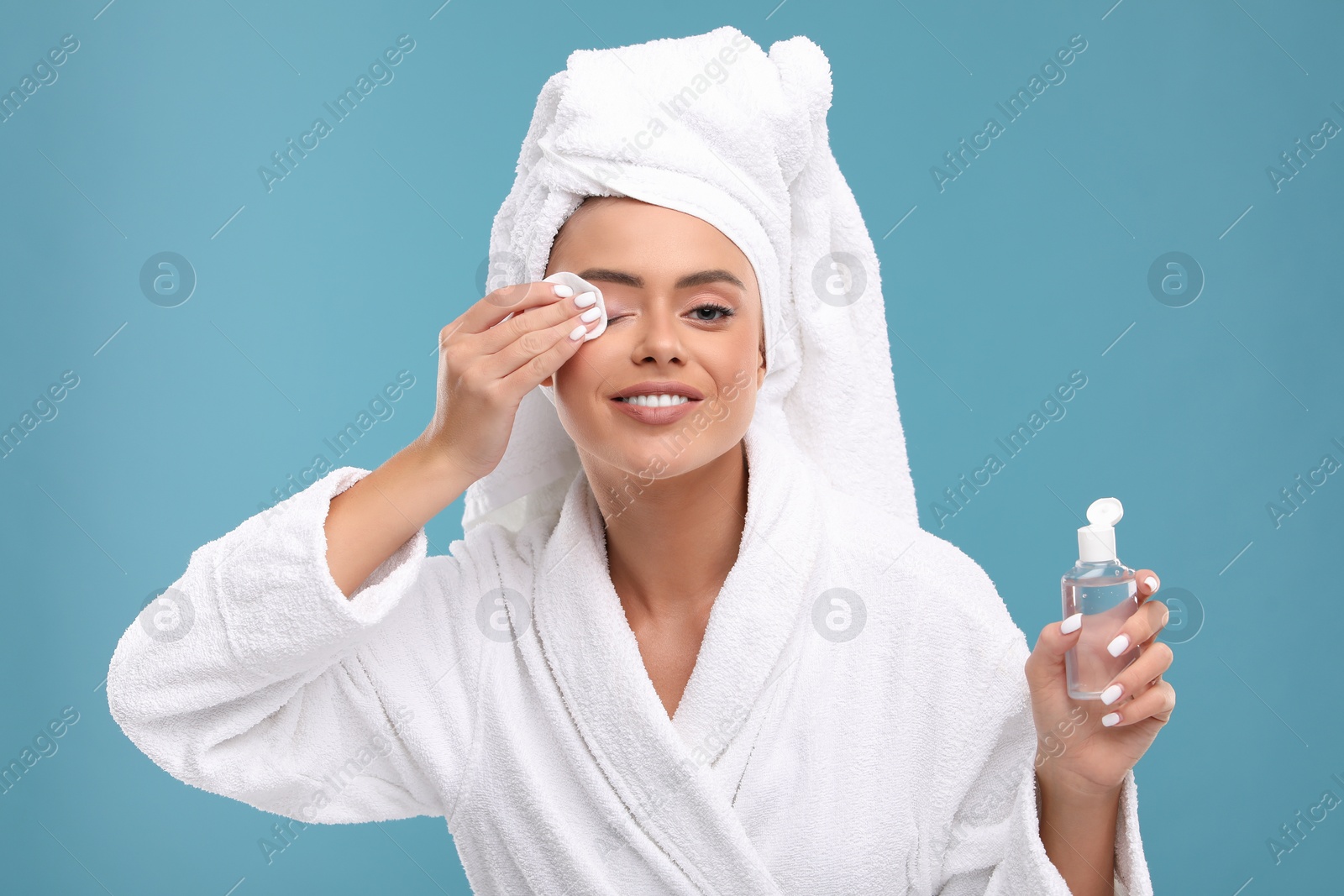 Photo of Beautiful woman removing makeup with cotton pad on light blue background