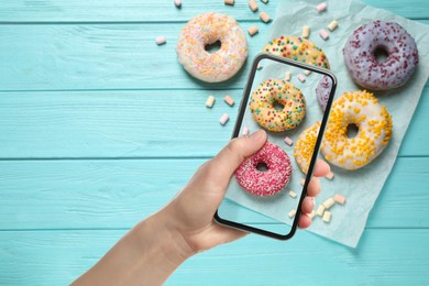 Image of Woman taking picture of tasty donuts on light blue wooden table, top view