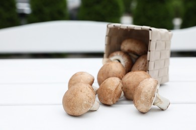 Photo of Overturned basket with fresh champignon mushrooms on white wooden table outdoors, space for text