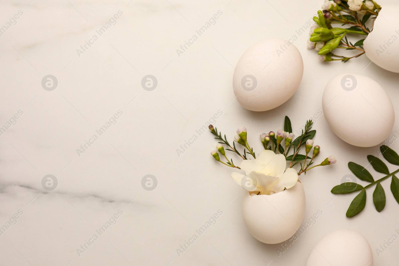 Photo of Easter eggs and beautiful flowers on white marble table, flat lay. Space for text