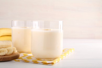 Photo of Tasty yogurt in glasses and bananas on white wooden table, closeup. Space for text