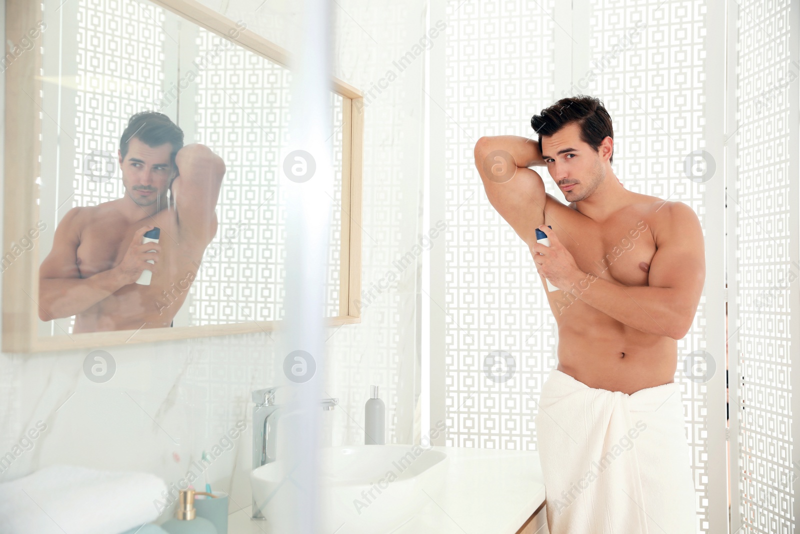 Photo of Handsome young man applying deodorant in bathroom