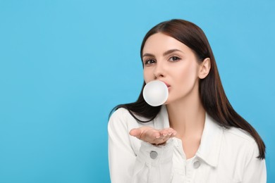 Photo of Beautiful woman blowing bubble gum on light blue background, space for text