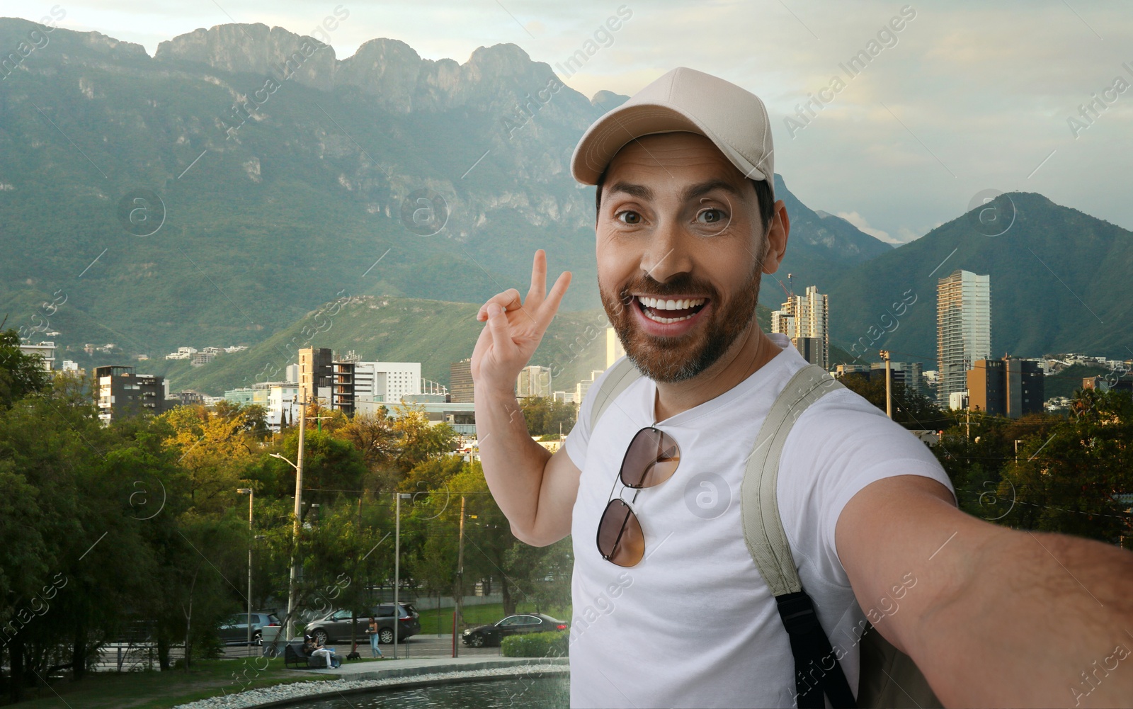 Image of Smiling man taking selfie and showing peace sign against cityscape
