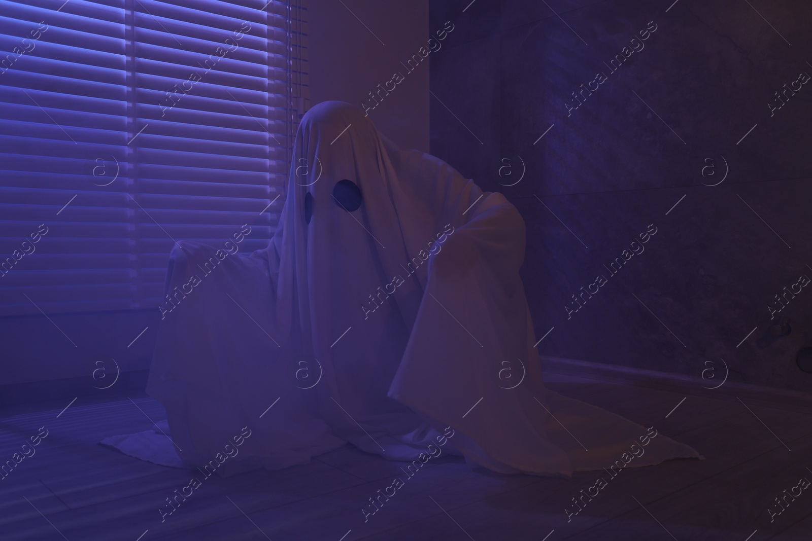 Photo of Creepy ghost. Woman covered with sheet near window in color lights