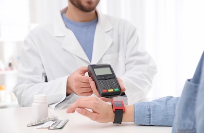 Photo of Woman using terminal for contactless payment with smartwatch in pharmacy, closeup