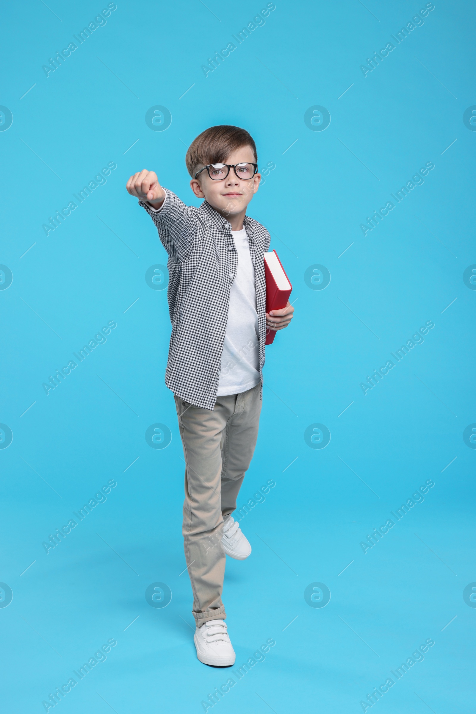 Photo of Cute schoolboy in glasses with book on light blue background