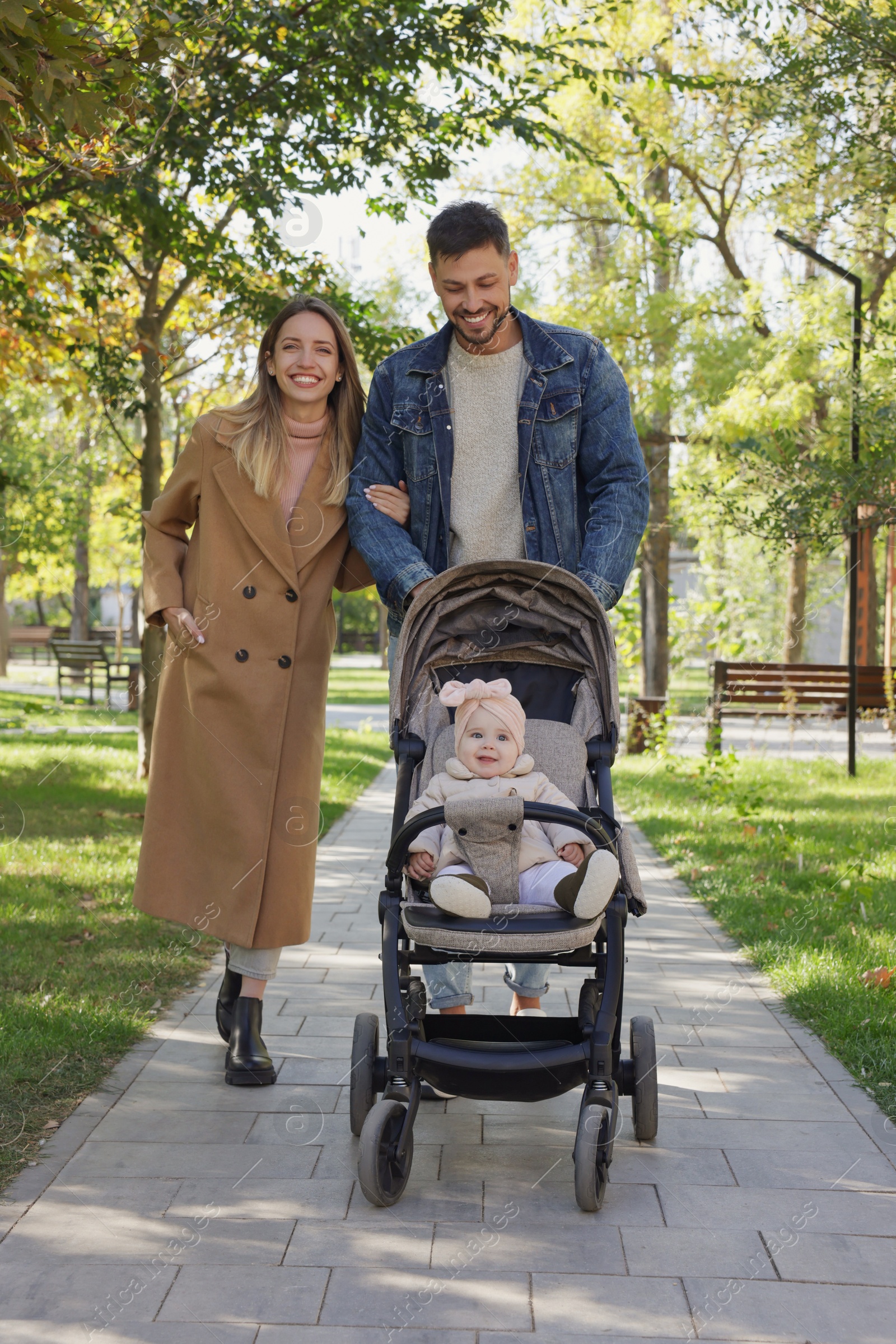 Photo of Happy parents walking with their baby in stroller at park on sunny day