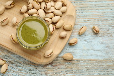 Photo of Delicious pistachio butter and ingredients on light blue wooden table, flat lay