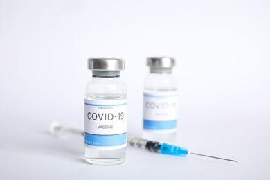 Vials with coronavirus vaccine and syringe on white background