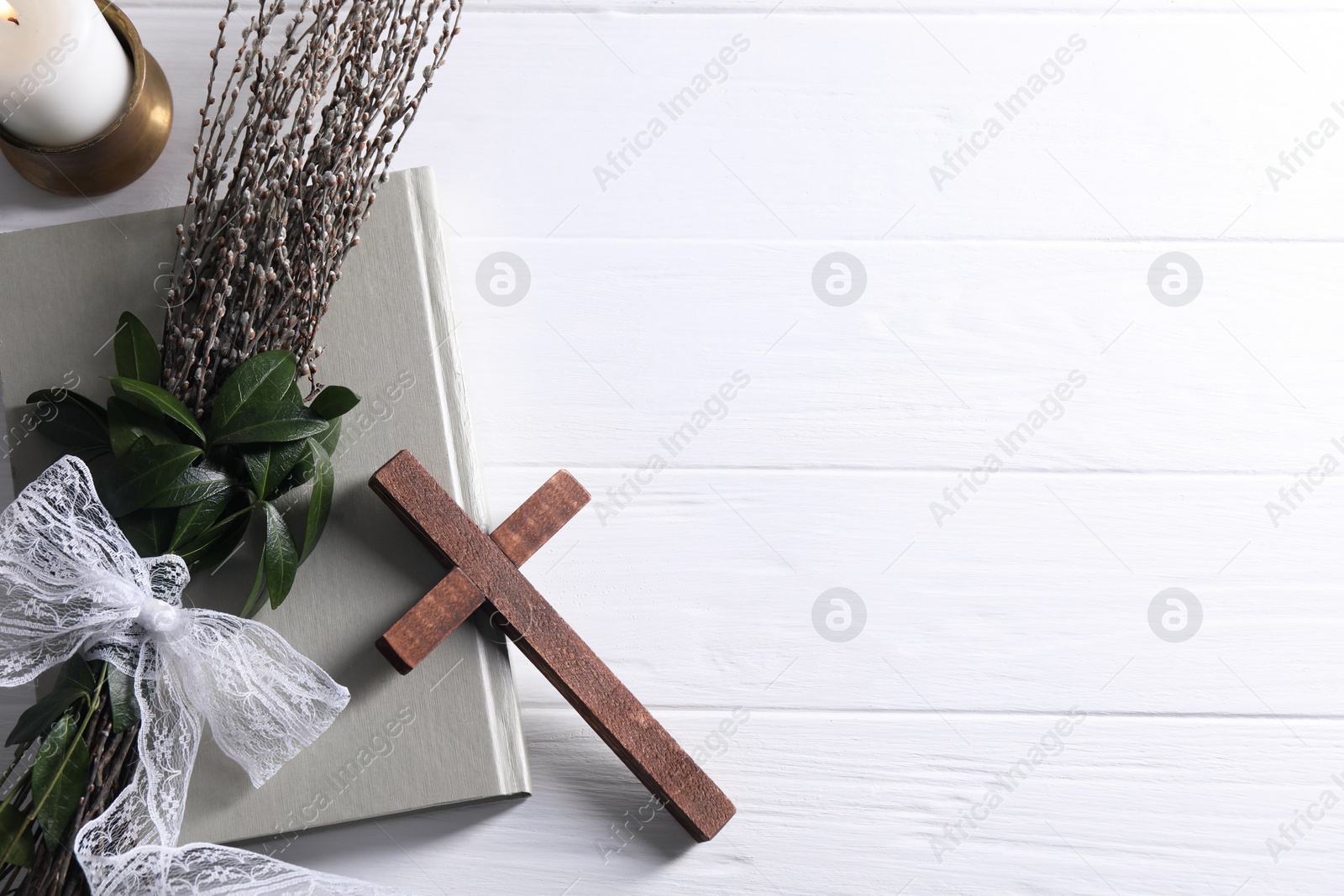 Photo of Burning candle, bouquet with willow branches, book and cross on white wooden table, flat lay. Space for text