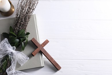 Burning candle, bouquet with willow branches, book and cross on white wooden table, flat lay. Space for text