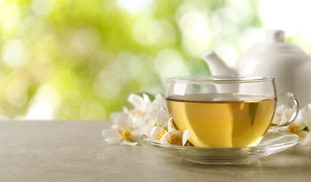 Image of Cup of jasmine tea and fresh flowers on grey table outdoors, space for text. Banner design