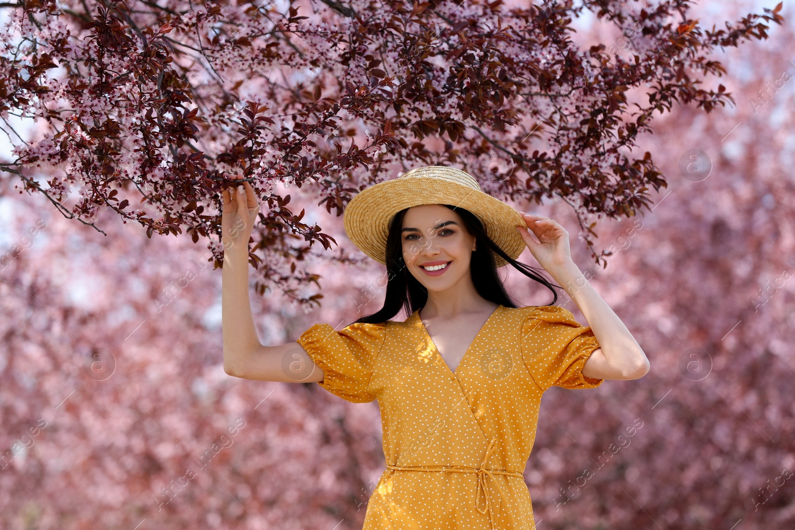 Photo of Pretty young woman with straw hat near beautiful blossoming trees outdoors. Stylish spring look