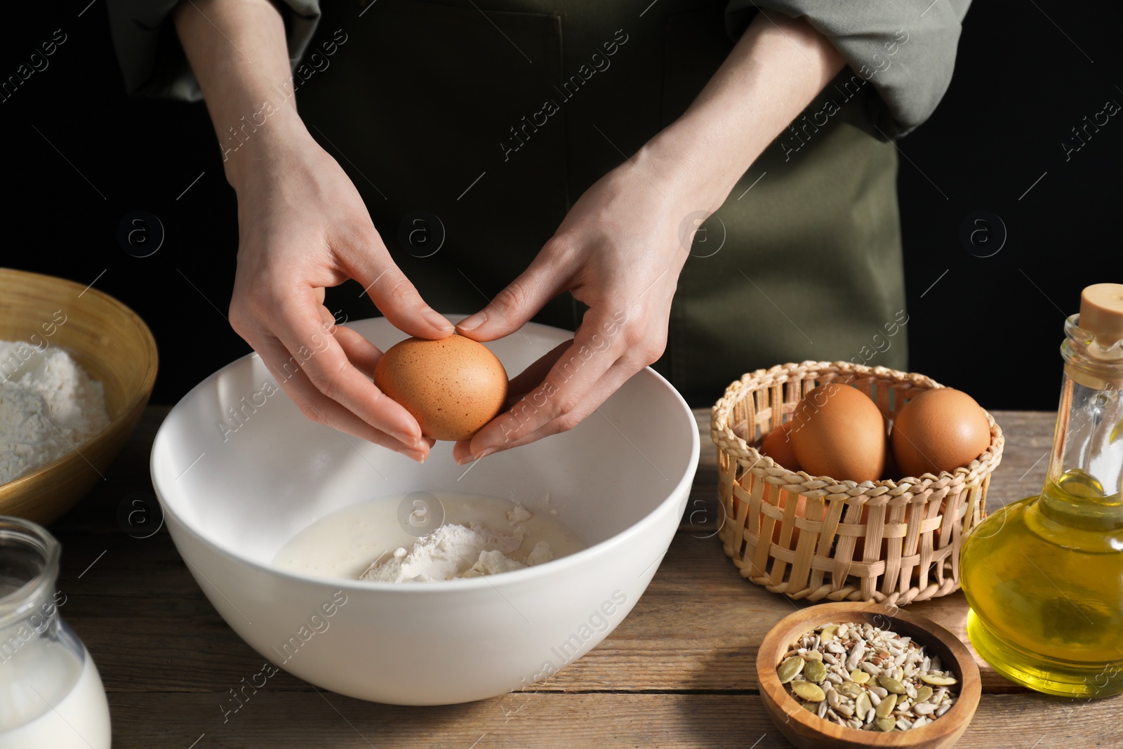 Photo of Making bread. Woman adding egg into dough at wooden table on dark background, closeup