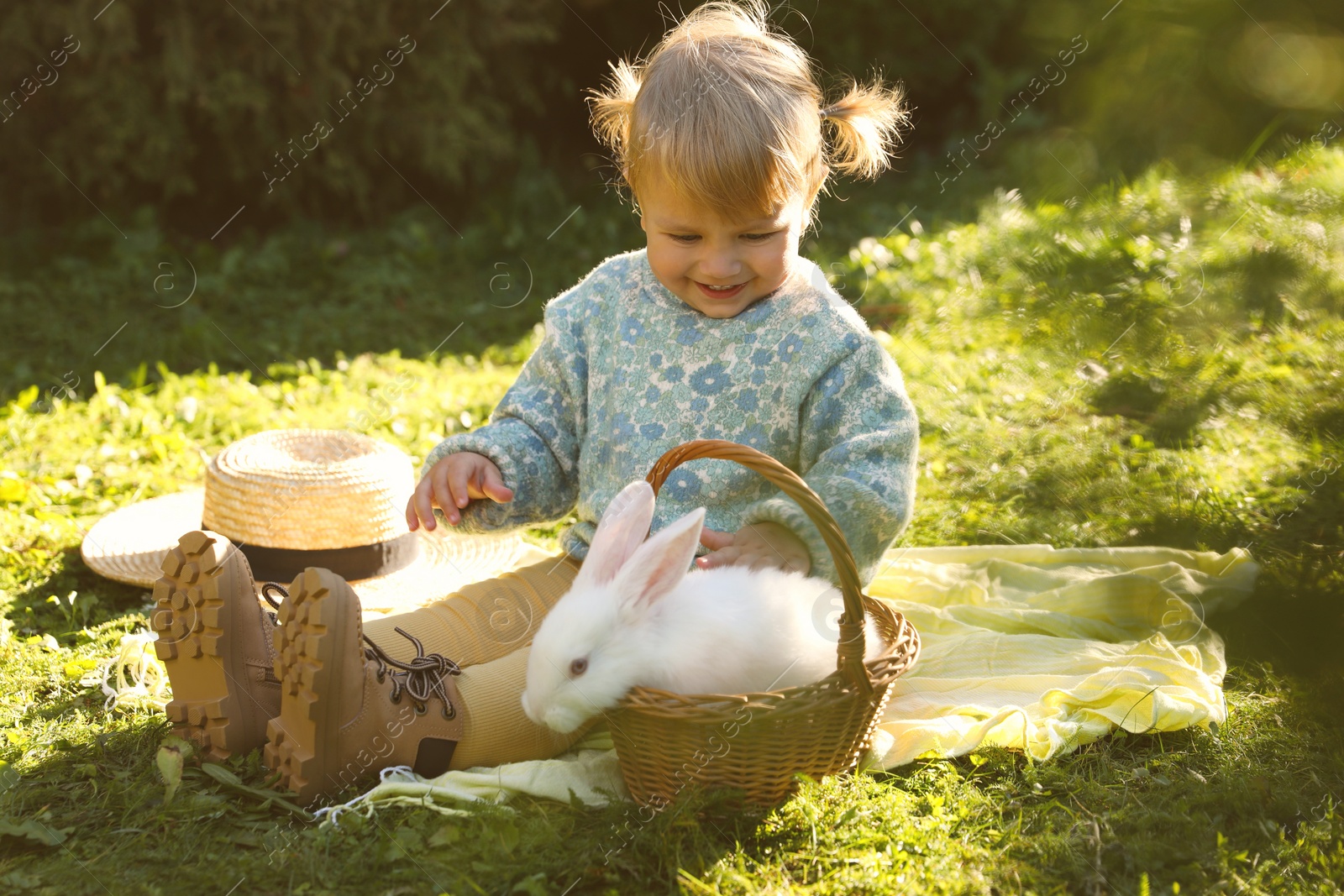 Photo of Happy little girl with cute rabbit on green grass outdoors