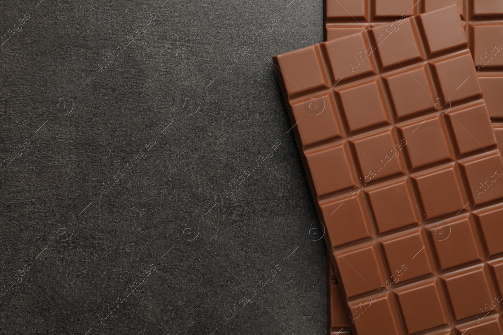 Photo of Delicious milk chocolate bars on black table, flat lay. Space for text