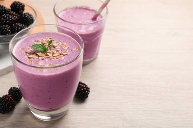 Photo of Delicious blackberry smoothie with oatmeal in glass on white wooden table, space for text