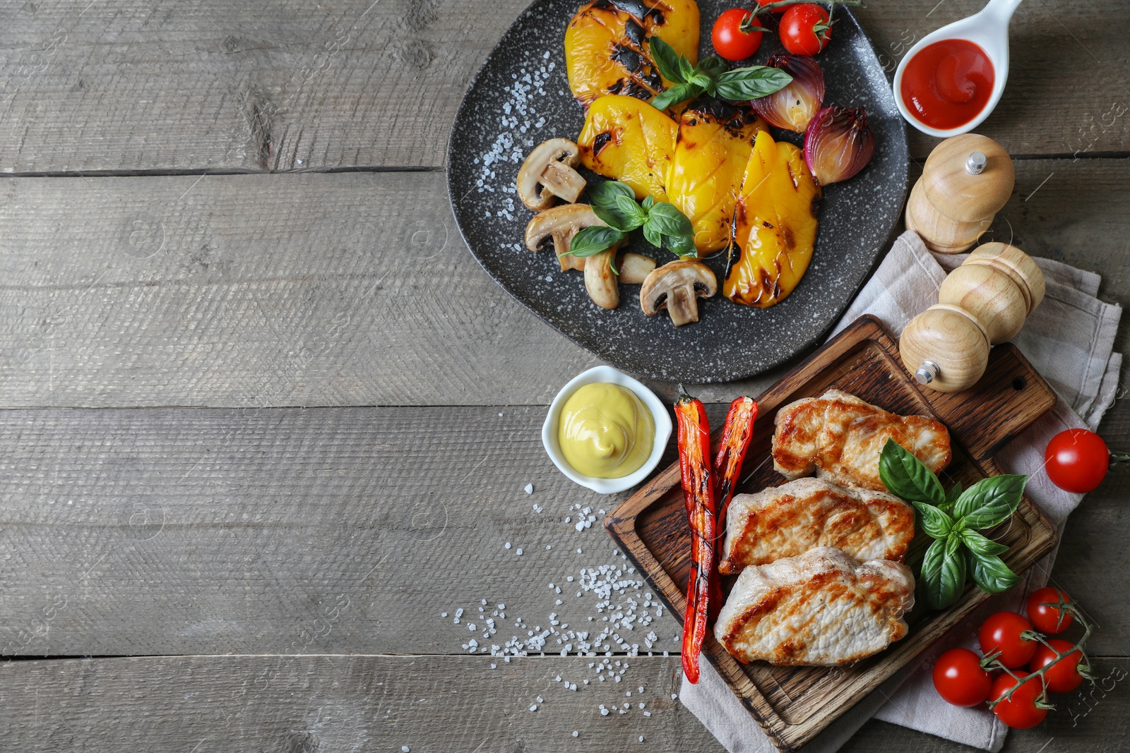 Photo of Delicious grilled meat and vegetables served with sauces on wooden table, flat lay. Space for text