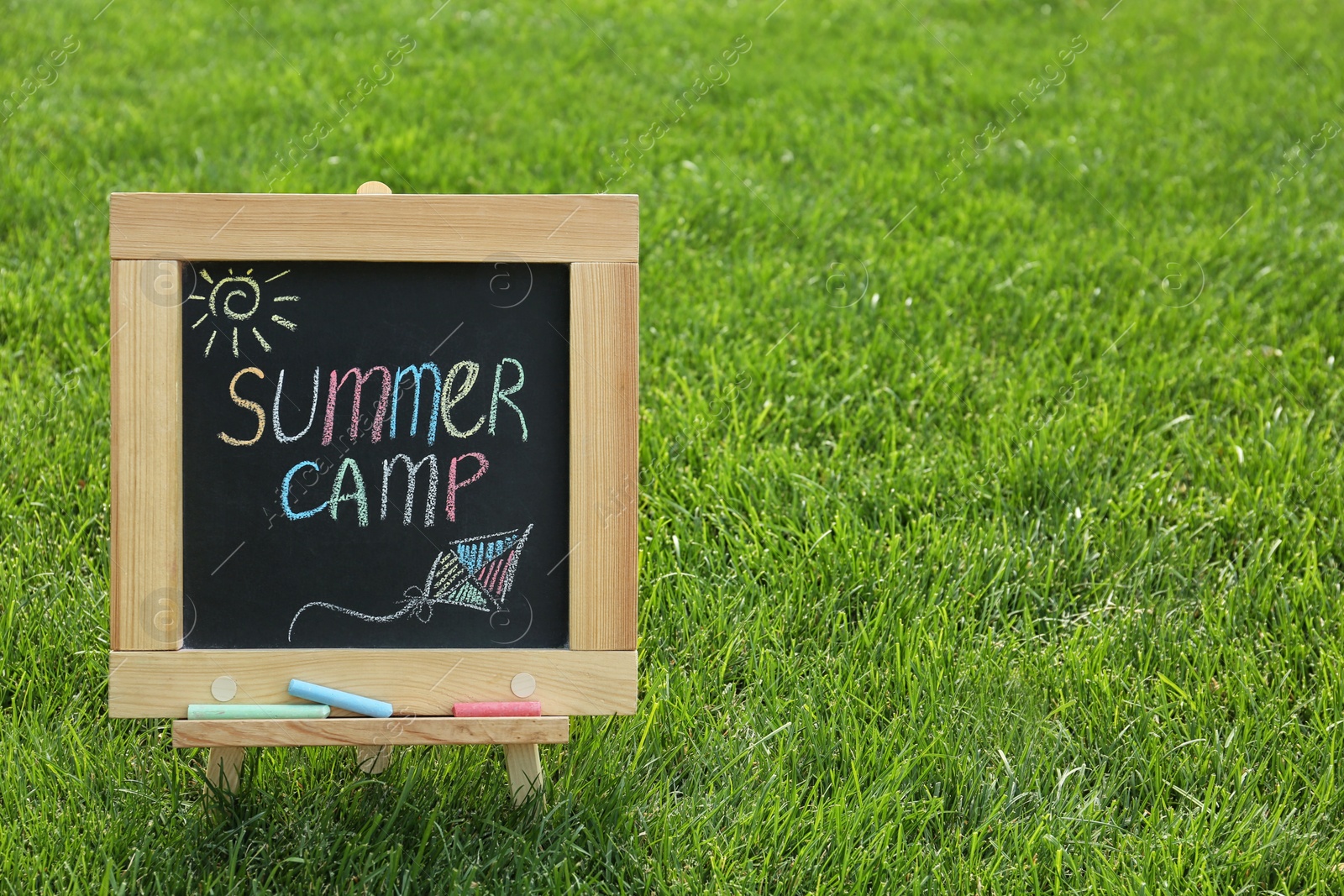 Photo of Blackboard with text SUMMER CAMP and drawings on green grass. Space for text