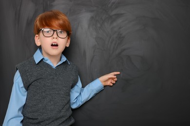 Photo of Cute schoolboy pointing at something on blackboard. Space for text