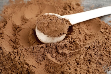 Photo of Pile of chocolate protein powder and scoop on grey table, closeup