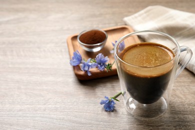Photo of Glass cup of delicious chicory drink and flowers on wooden table, closeup. Space for text
