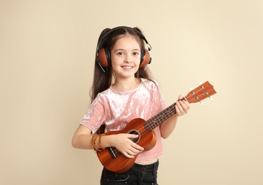 Photo of Portrait of little cheerful girl with headphones playing guitar on color background