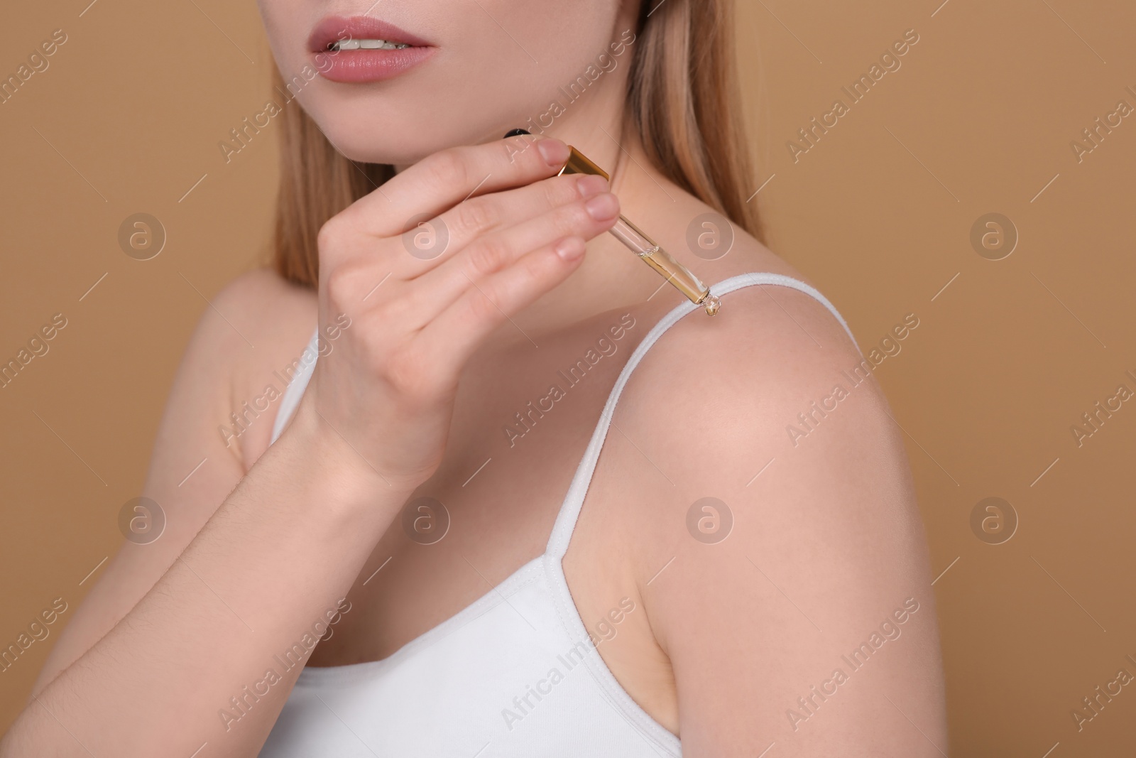 Photo of Woman applying essential oil onto shoulder on brown background, closeup