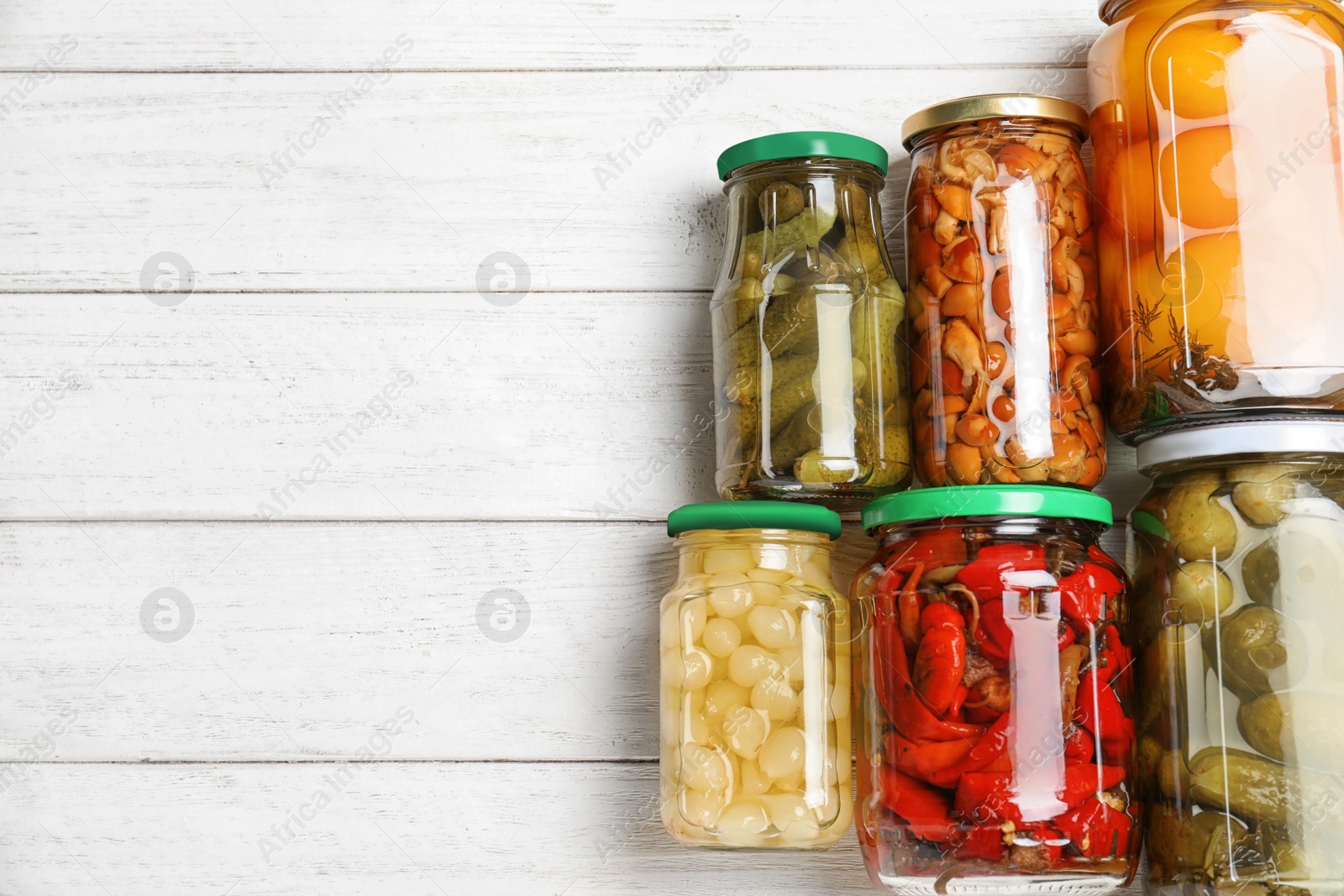 Photo of Glass jars with different pickled vegetables on white wooden table, flat lay. Space for text