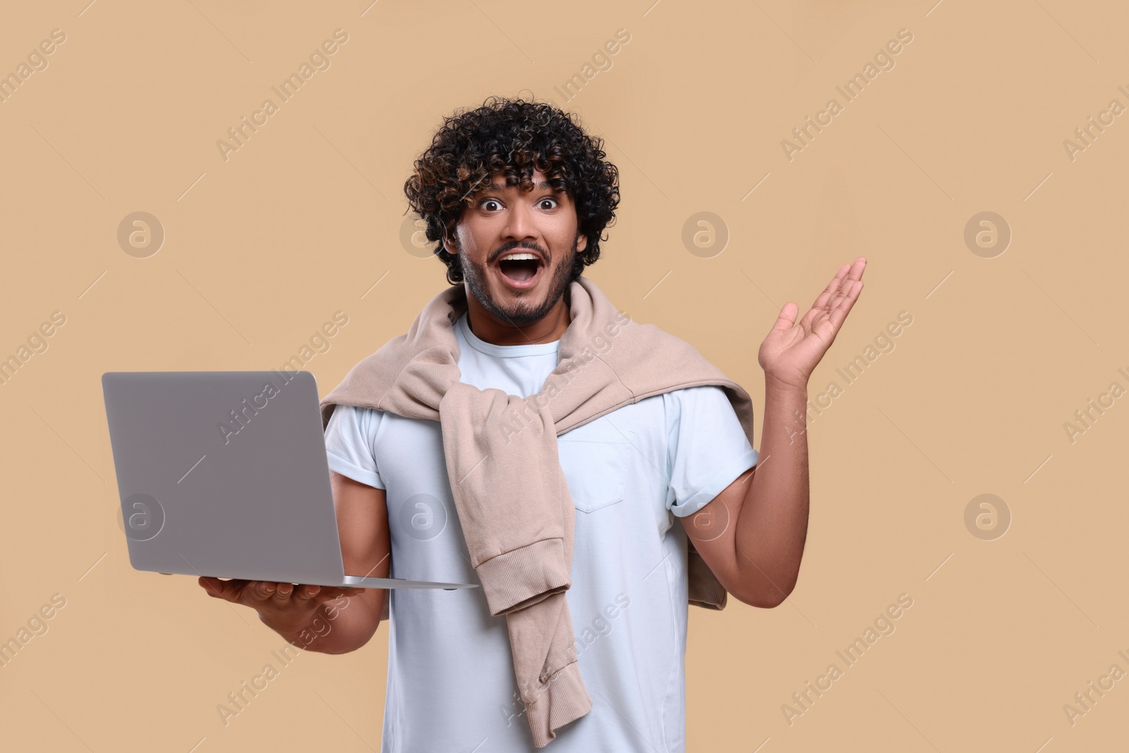 Photo of Surprised man with laptop on beige background. Space for text