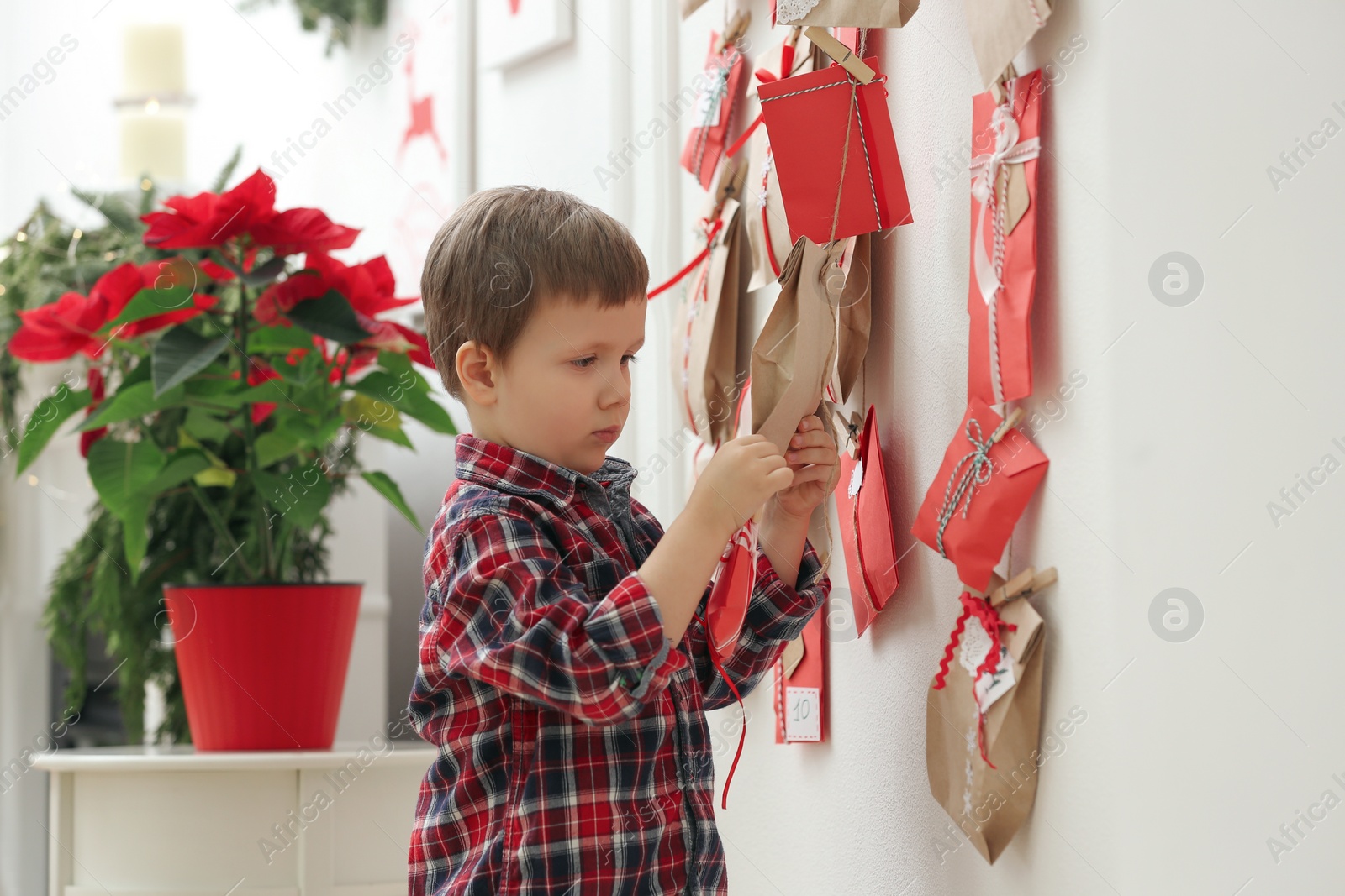 Photo of Cute little boy taking gift from Advent calendar at home. Christmas tradition