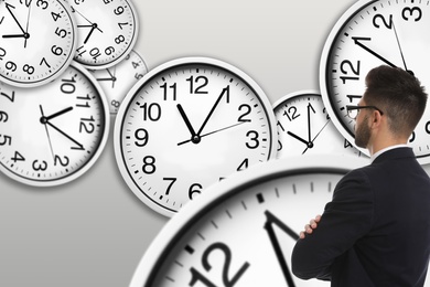Image of Time management concept. Businessman standing in front of clocks on light background, back view