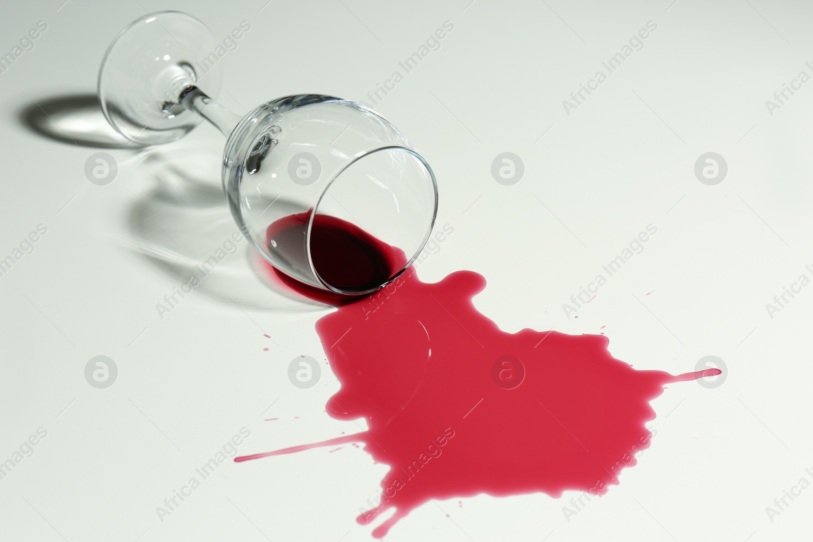 Photo of Overturned glass and spilled wine on white background