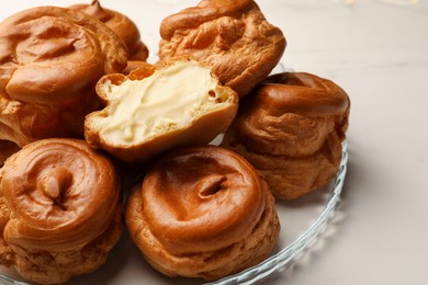 Photo of Delicious profiteroles with cream filling inside on white table