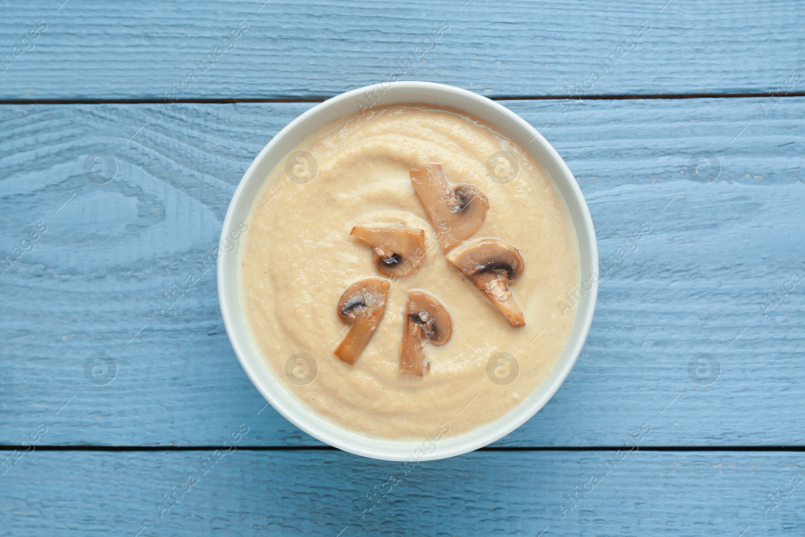 Photo of Delicious mushroom cream soup on light grey wooden table, top view