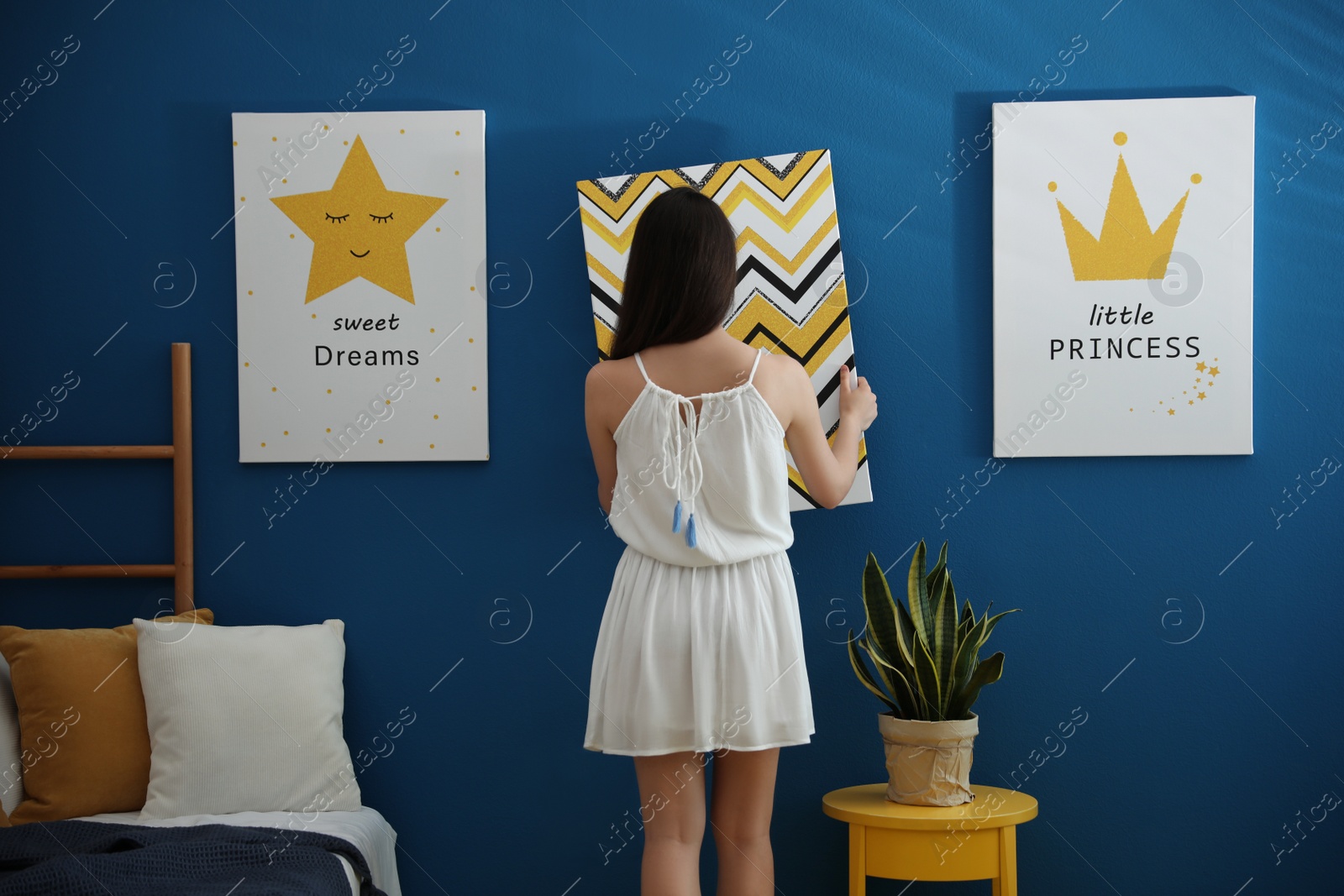 Photo of Decorator hanging picture on blue wall. Children's room interior design