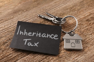 Photo of Inheritance Tax. Card and keys with key chain in shape of house on wooden table, closeup
