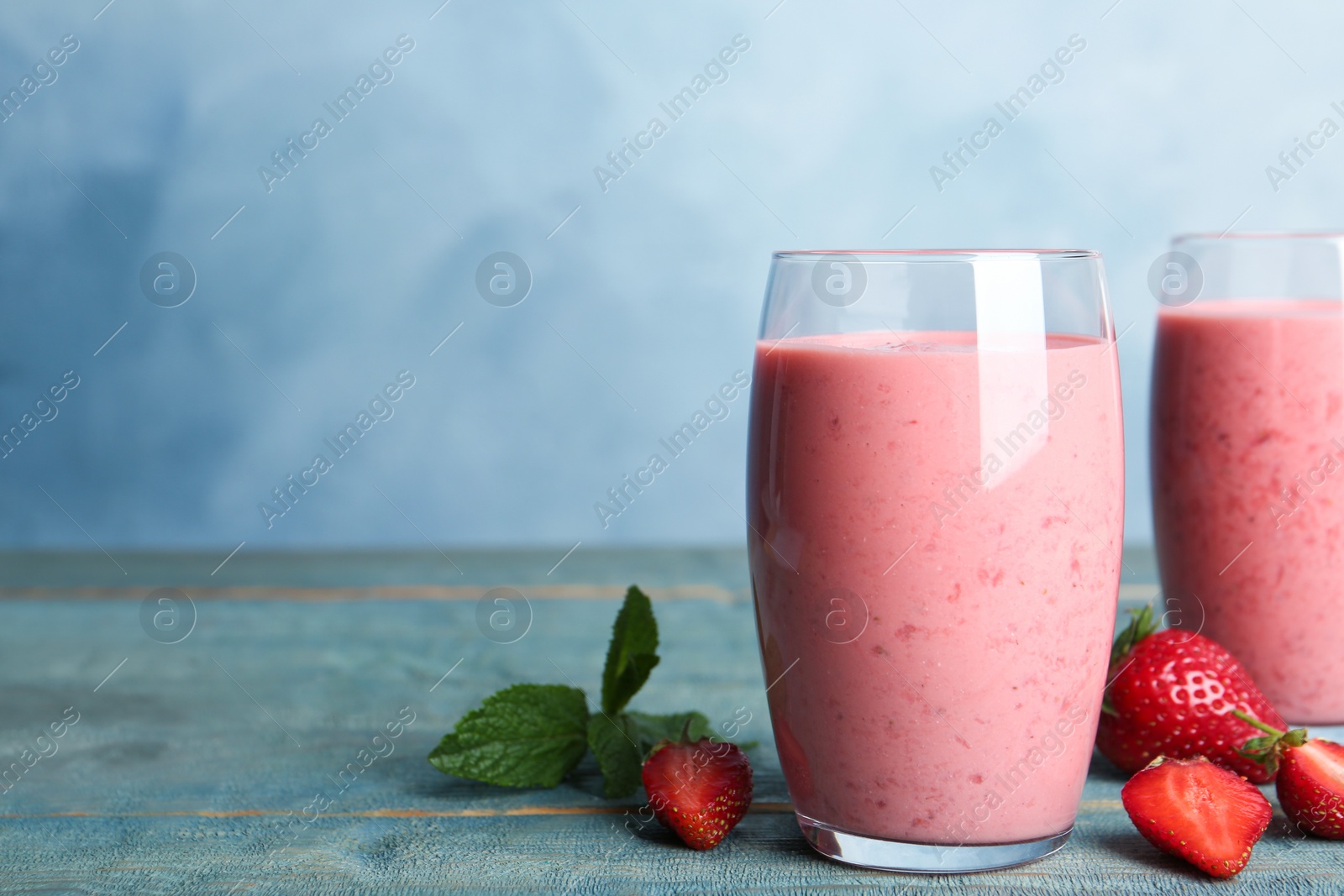 Photo of Tasty strawberry smoothies in glasses on blue wooden table. Space for text