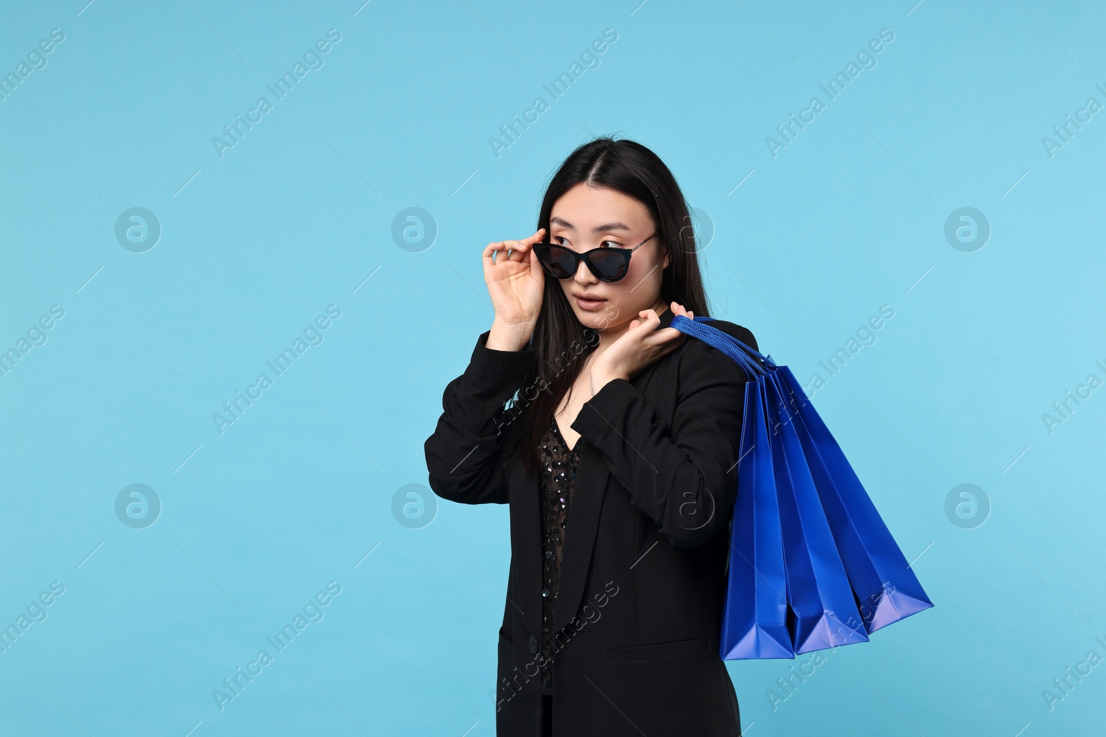 Photo of Beautiful woman with shopping bags on light blue background. Space for text