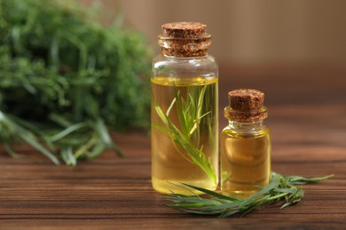 Photo of Bottles of essential oil and fresh tarragon leaves on wooden table