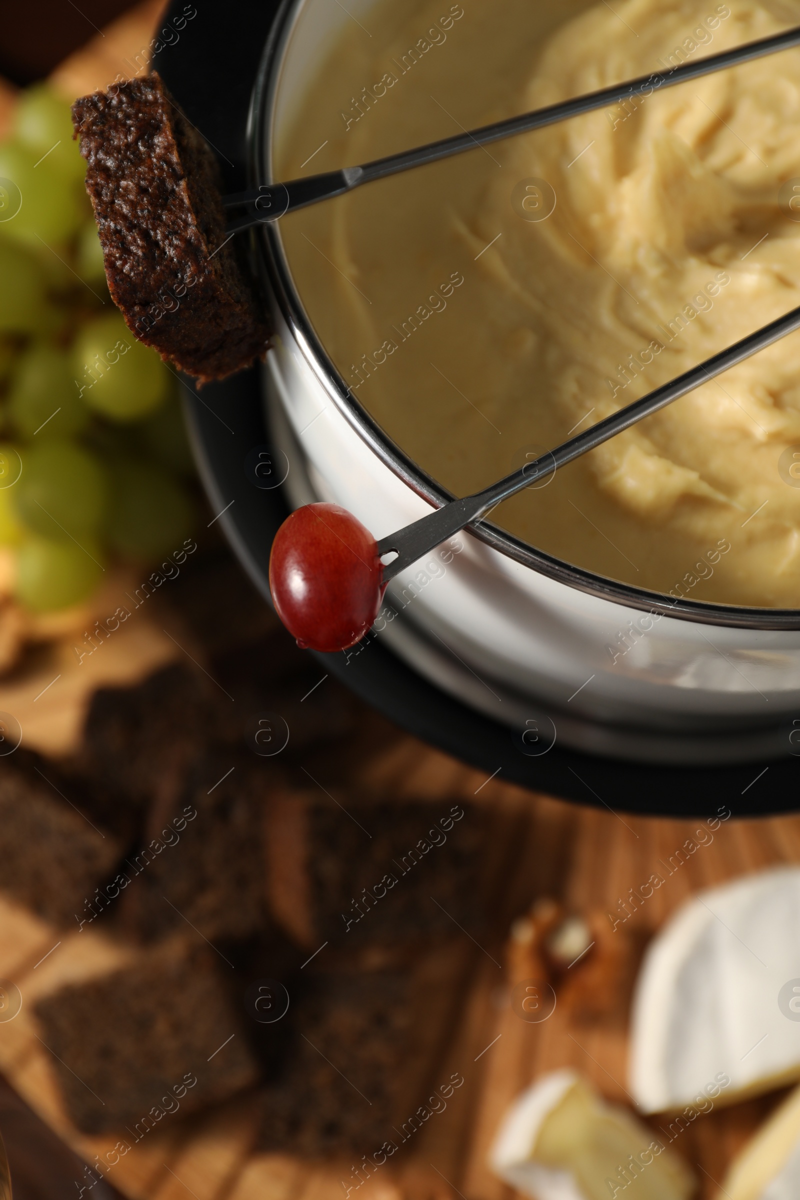 Photo of Forks with pieces of grape, bread, fondue pot with melted cheese and snacks on table, above view