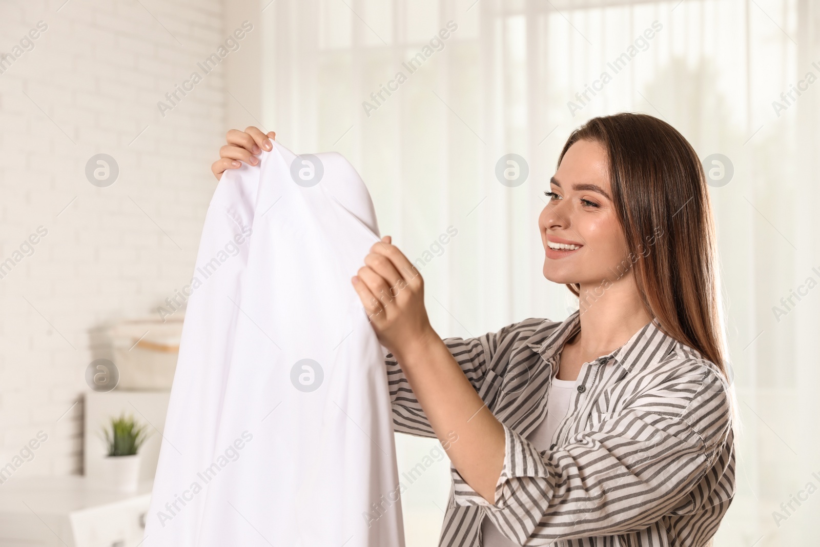 Photo of Happy young woman with clean shirt indoors. Laundry day